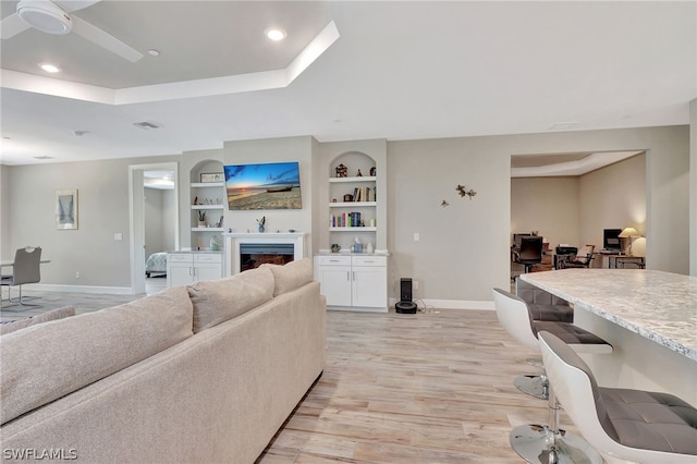 living room with ceiling fan, built in features, and light hardwood / wood-style flooring