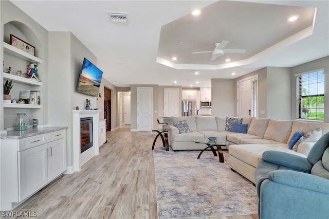 living room with a tray ceiling, ceiling fan, and light hardwood / wood-style flooring