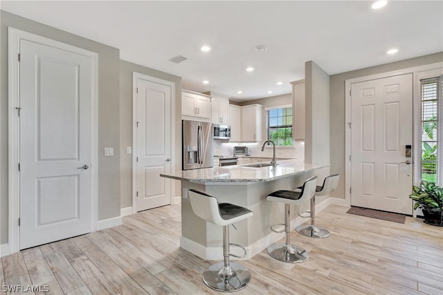 kitchen with white cabinets, sink, light wood-type flooring, light stone counters, and stainless steel appliances