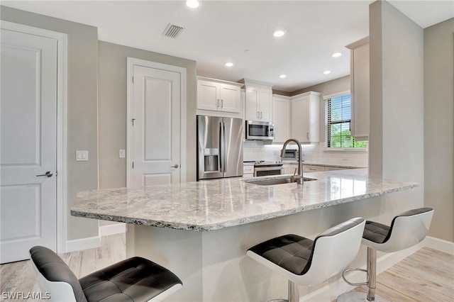 kitchen with sink, light stone counters, light hardwood / wood-style floors, white cabinets, and appliances with stainless steel finishes