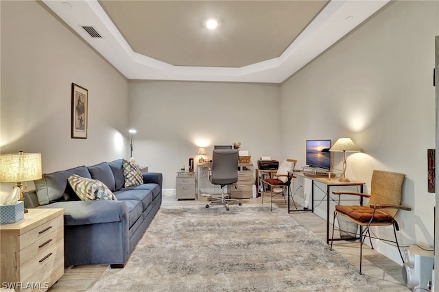 home office with a raised ceiling and light wood-type flooring