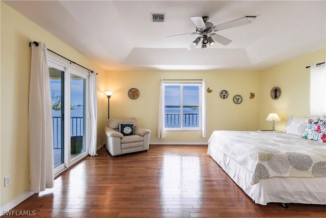 bedroom with access to outside, ceiling fan, dark wood-type flooring, and a tray ceiling