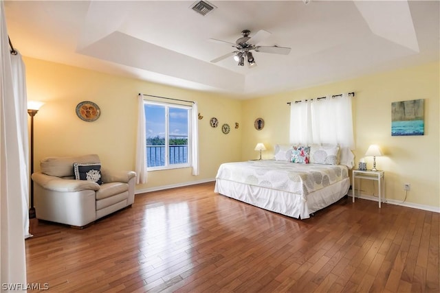 bedroom featuring ceiling fan, wood-type flooring, and a tray ceiling