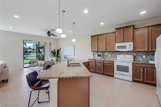 kitchen with pendant lighting, white appliances, sink, ceiling fan, and an island with sink