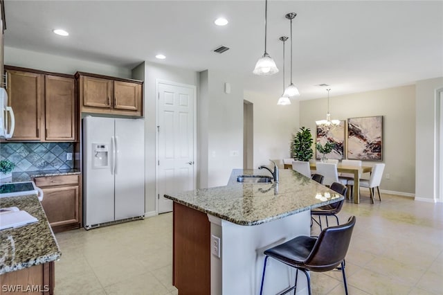 kitchen with light stone countertops, an island with sink, a chandelier, decorative light fixtures, and white appliances