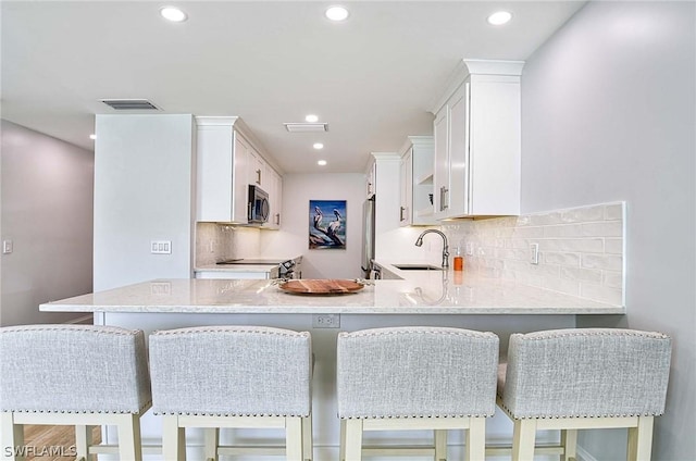 kitchen featuring white cabinets, a kitchen breakfast bar, sink, kitchen peninsula, and stainless steel appliances