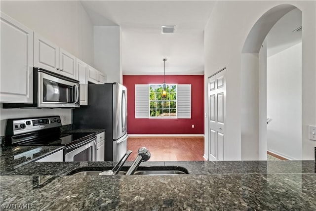 kitchen featuring stainless steel appliances, hanging light fixtures, dark stone countertops, and white cabinets