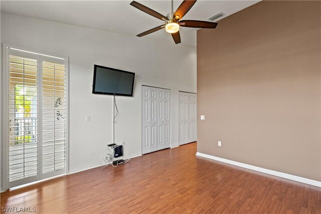 unfurnished living room featuring hardwood / wood-style flooring, ceiling fan, and a high ceiling