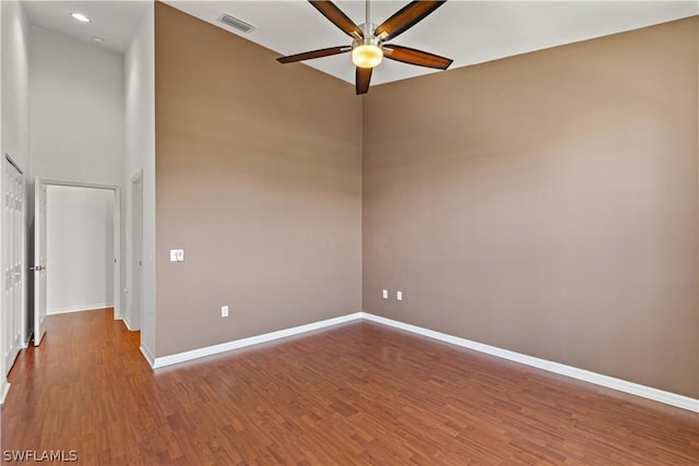 empty room with a towering ceiling, hardwood / wood-style floors, and ceiling fan