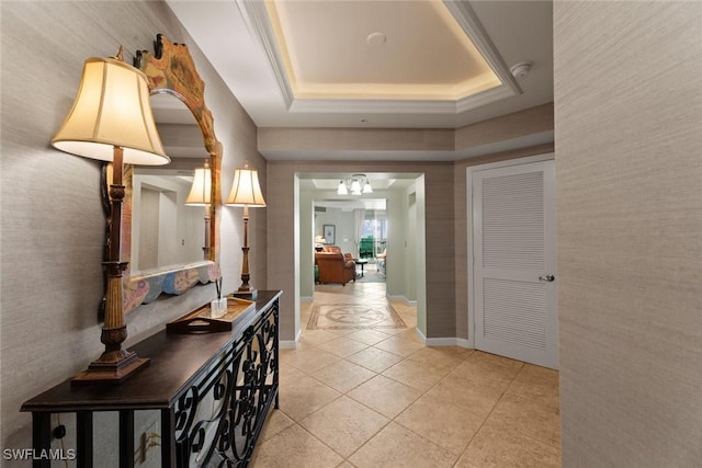 hall with a raised ceiling, a chandelier, light tile patterned floors, and baseboards