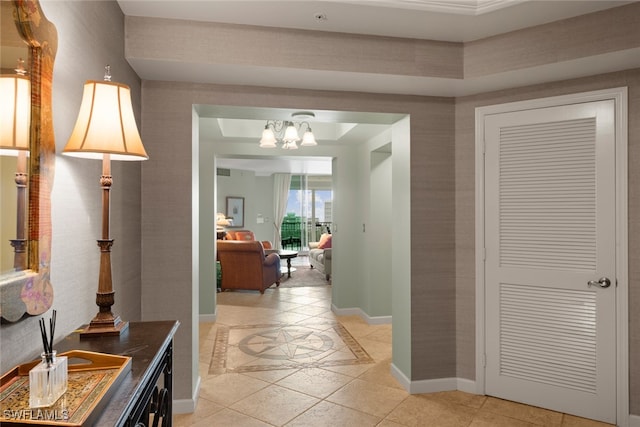 hallway with a chandelier, a tray ceiling, and light tile patterned floors