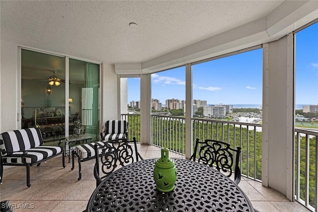 sunroom featuring a water view, ceiling fan, a textured ceiling, outdoor dining space, and a city view