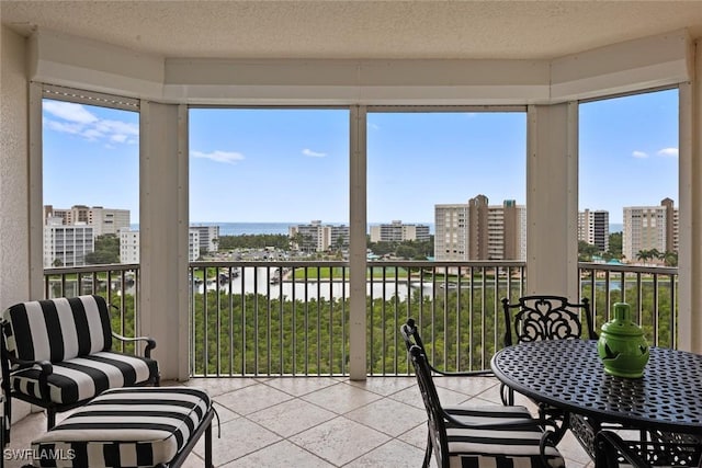 sunroom featuring a water view, a city view, a textured ceiling, tile patterned floors, and healthy amount of natural light