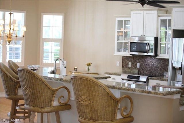 kitchen with white cabinetry, appliances with stainless steel finishes, pendant lighting, light stone countertops, and backsplash