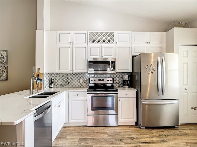 kitchen featuring white cabinetry, light stone countertops, stainless steel appliances, kitchen peninsula, and vaulted ceiling