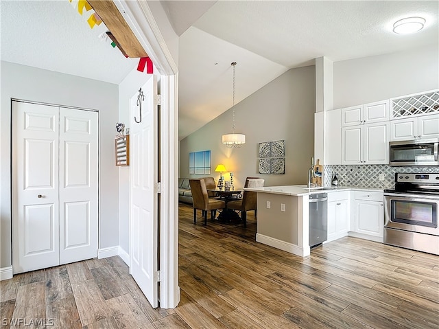 kitchen with backsplash, stainless steel appliances, vaulted ceiling, pendant lighting, and white cabinetry