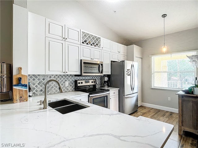 kitchen with sink, vaulted ceiling, light stone countertops, appliances with stainless steel finishes, and decorative light fixtures