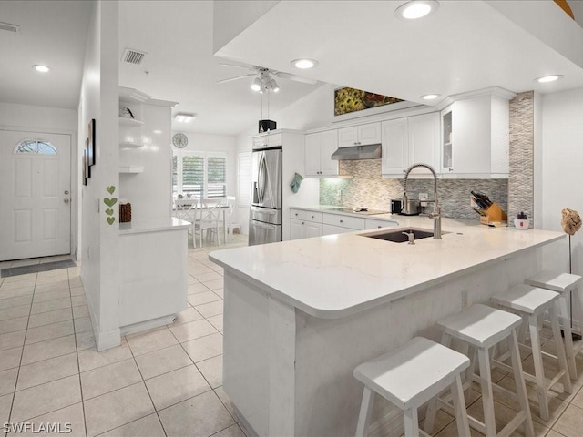 kitchen with sink, white cabinetry, a kitchen breakfast bar, stainless steel fridge, and kitchen peninsula