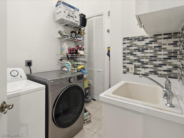 laundry area featuring light tile patterned flooring, washing machine and clothes dryer, and sink