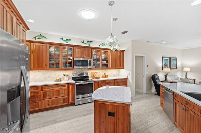 kitchen with light hardwood / wood-style flooring, a center island, hanging light fixtures, tasteful backsplash, and appliances with stainless steel finishes