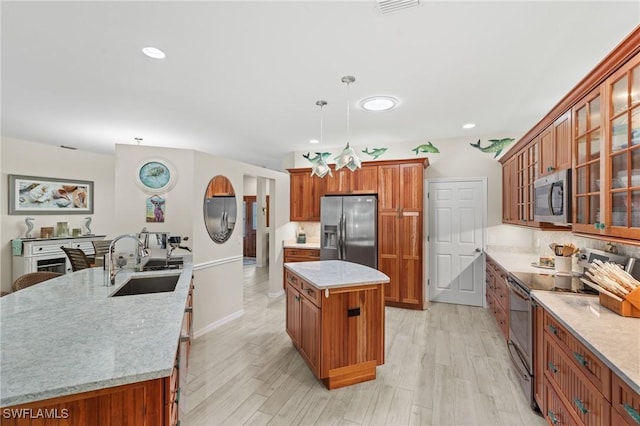 kitchen with light hardwood / wood-style flooring, hanging light fixtures, a center island, appliances with stainless steel finishes, and sink