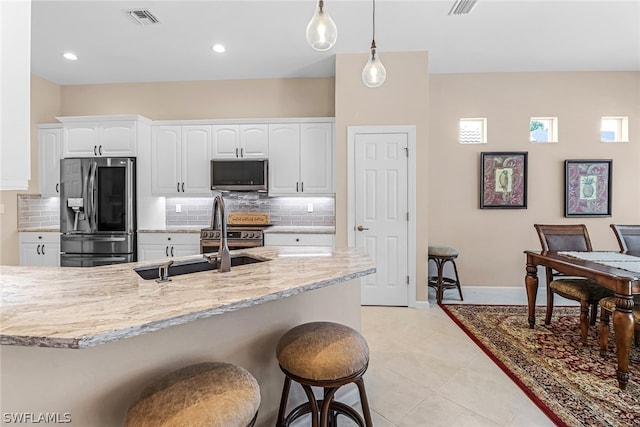 kitchen featuring light stone counters, stainless steel appliances, pendant lighting, light tile patterned floors, and white cabinets