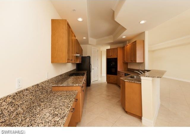 kitchen with double oven, stone countertops, a tray ceiling, sink, and light tile floors