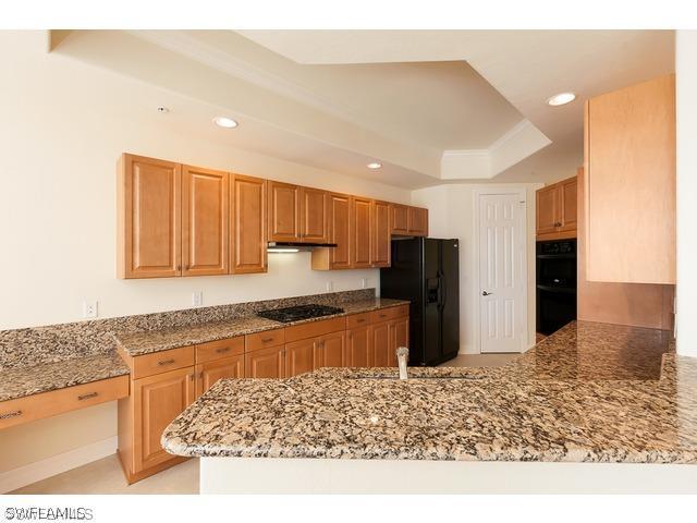 kitchen featuring a raised ceiling, black appliances, kitchen peninsula, and light stone countertops