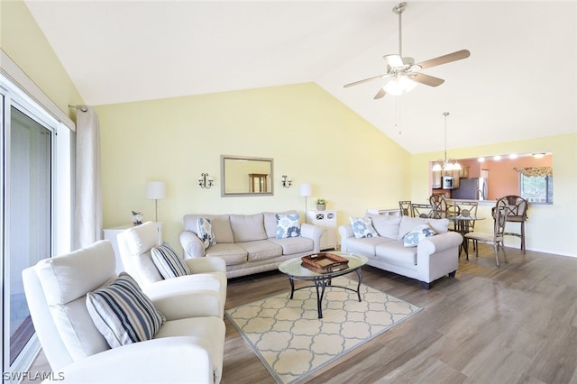 living room with wood-type flooring, ceiling fan with notable chandelier, vaulted ceiling, and a wealth of natural light