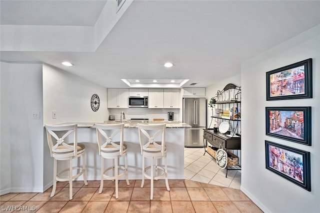 kitchen featuring stainless steel appliances, white cabinetry, a raised ceiling, light tile patterned floors, and a breakfast bar