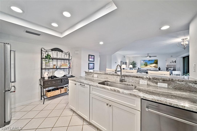 kitchen with sink, stainless steel appliances, white cabinets, light stone counters, and ceiling fan with notable chandelier