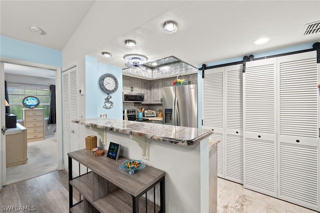 kitchen with a barn door, visible vents, appliances with stainless steel finishes, a breakfast bar area, and a peninsula