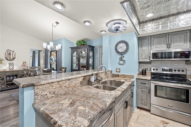 kitchen with appliances with stainless steel finishes, decorative light fixtures, a sink, light stone countertops, and backsplash