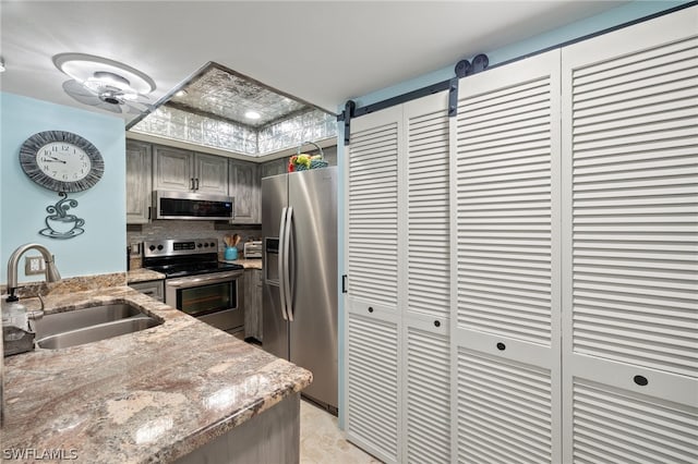 kitchen with a barn door, decorative backsplash, light stone countertops, stainless steel appliances, and a sink