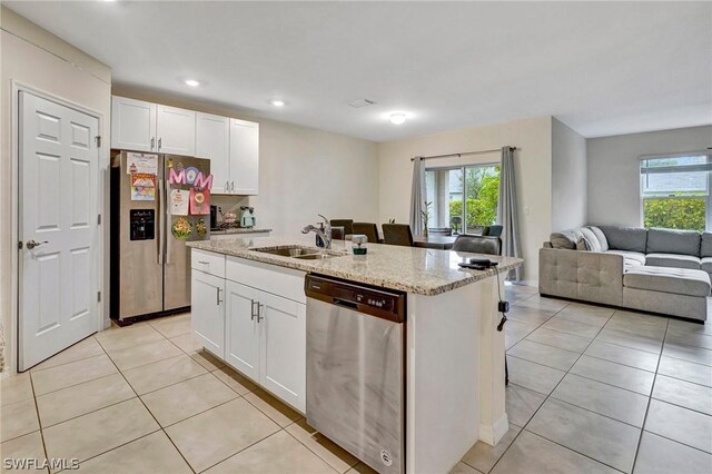 kitchen featuring light stone counters, stainless steel appliances, a center island with sink, white cabinets, and light tile floors