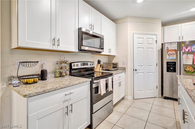 kitchen with stainless steel appliances, white cabinets, light tile floors, and light stone counters