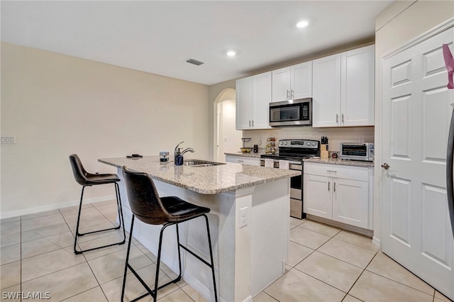 kitchen featuring stainless steel appliances, a center island with sink, light tile flooring, sink, and white cabinets