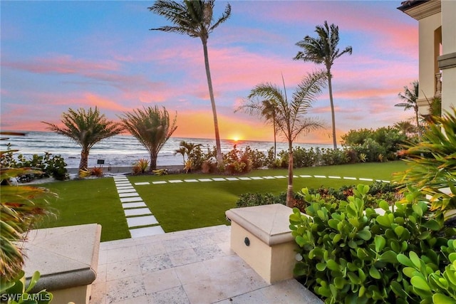 patio terrace at dusk featuring a lawn and a water view