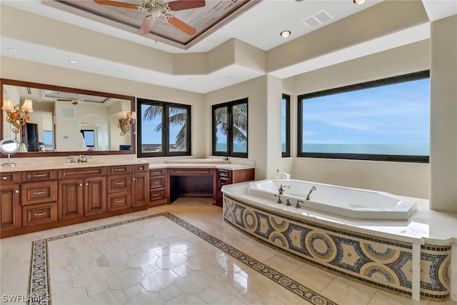 bathroom featuring ceiling fan, vanity, a tray ceiling, and tiled bath