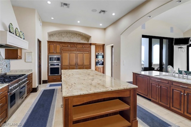 kitchen with sink, light tile patterned floors, stainless steel appliances, a center island, and light stone counters