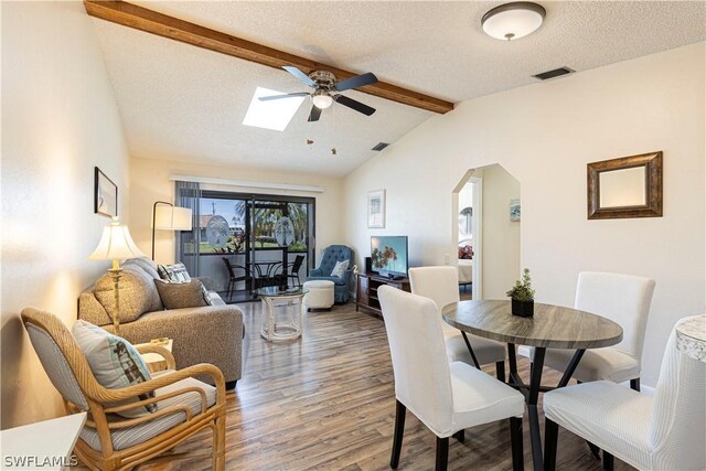 dining area featuring ceiling fan, wood-type flooring, lofted ceiling with skylight, and a textured ceiling