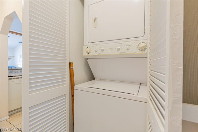 laundry area featuring stacked washer / drying machine and light tile patterned flooring