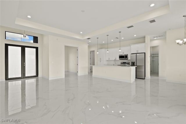 unfurnished living room featuring sink, a notable chandelier, french doors, and a tray ceiling