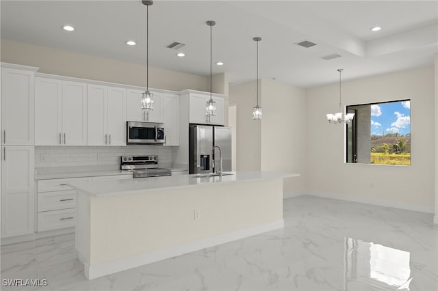 kitchen featuring white cabinets, tasteful backsplash, an island with sink, decorative light fixtures, and stainless steel appliances