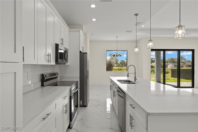 kitchen with sink, white cabinetry, stainless steel appliances, pendant lighting, and a center island with sink