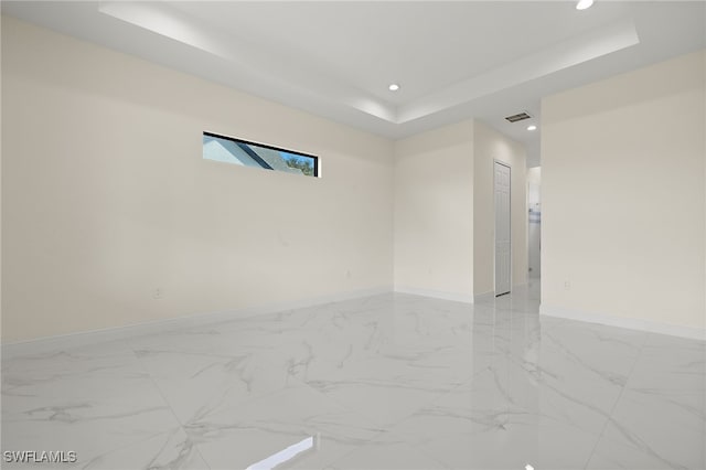 spare room featuring a tray ceiling, recessed lighting, baseboards, and light marble finish floors