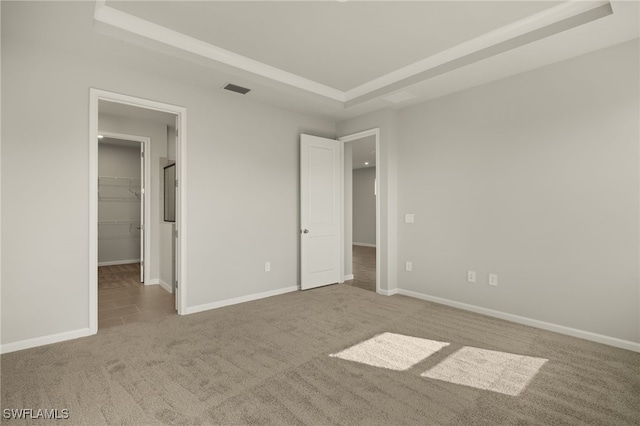 unfurnished bedroom featuring carpet flooring, a raised ceiling, a spacious closet, and a closet