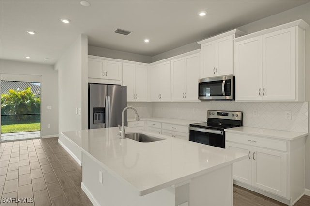 kitchen with white cabinetry, sink, stainless steel appliances, backsplash, and a kitchen island with sink