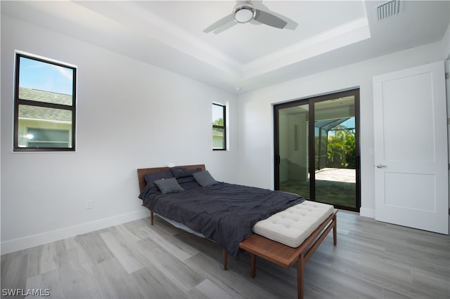 bedroom featuring multiple windows, a tray ceiling, access to outside, and light hardwood / wood-style flooring