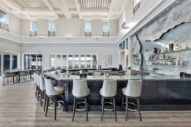 bar with coffered ceiling, light hardwood / wood-style flooring, beamed ceiling, and a high ceiling